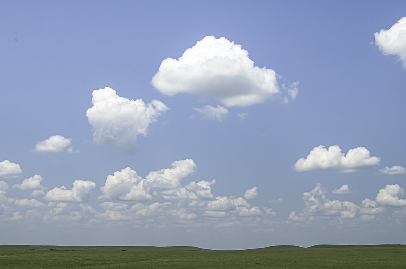 huge blue sky with white clouds over gently rolling green prairie landscape